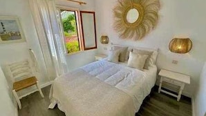 Un dormitorio con cama, mesita de noche, espejo y ventana con cortinas.