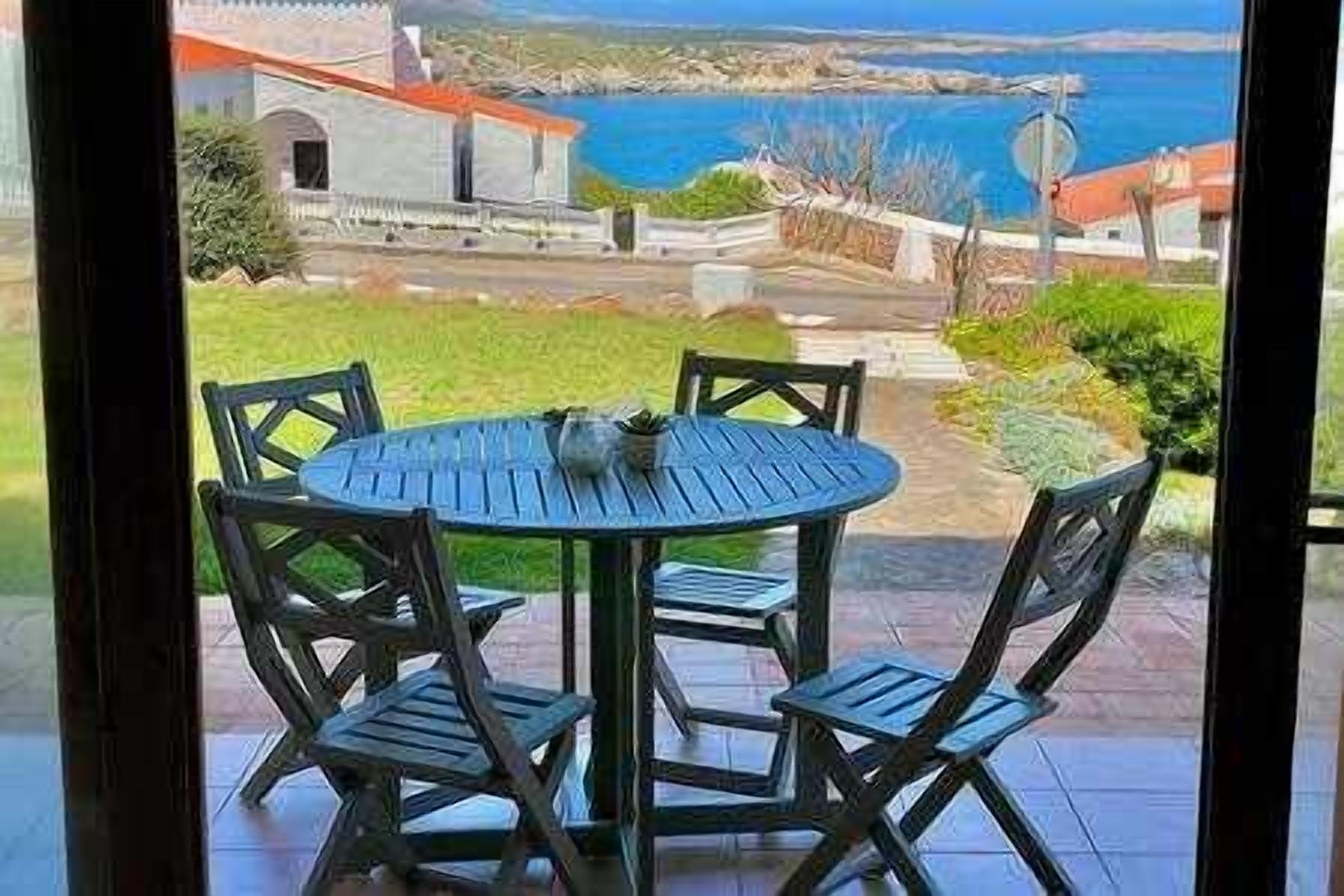 A round table with four chairs on a patio with a view of the sea and buildings.