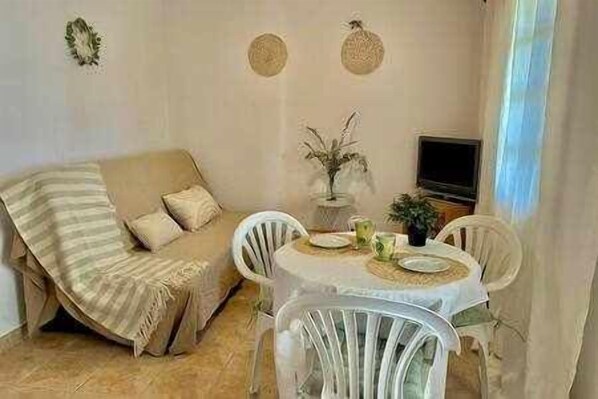 A living room with a sofa, a dining table with chairs, a TV, and a plant.