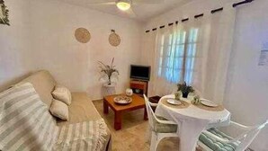 Una sala de estar con sofá, mesa de centro, televisor y mesa de comedor con sillas.