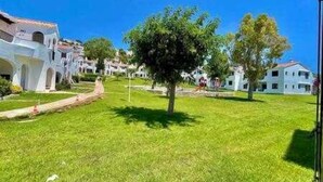 Un patio con césped y un árbol, rodeado de edificios blancos con tejas rojas.