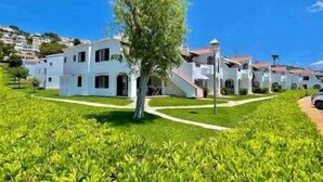 Una hilera de edificios blancos con un árbol central, rodeados de césped verde.