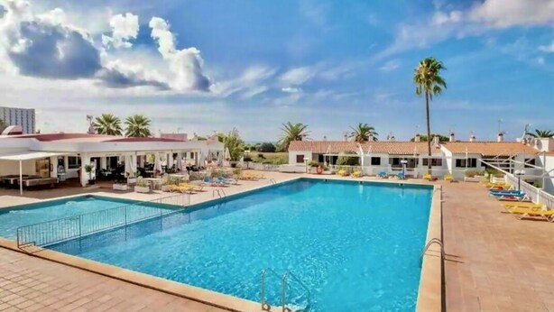 Una piscina con solárium de baldosas, palmeras y cielo despejado.