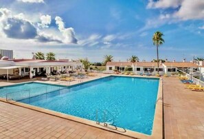A swimming pool with a tiled deck, palm trees, and a clear sky.