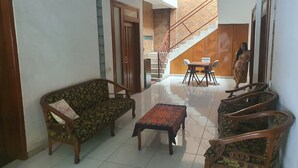 A living room with a sofa, a coffee table, and a dining area with chairs and a table. A staircase is visible in the background. - Hotel O Damia Homestay Syariah (Surabaya)