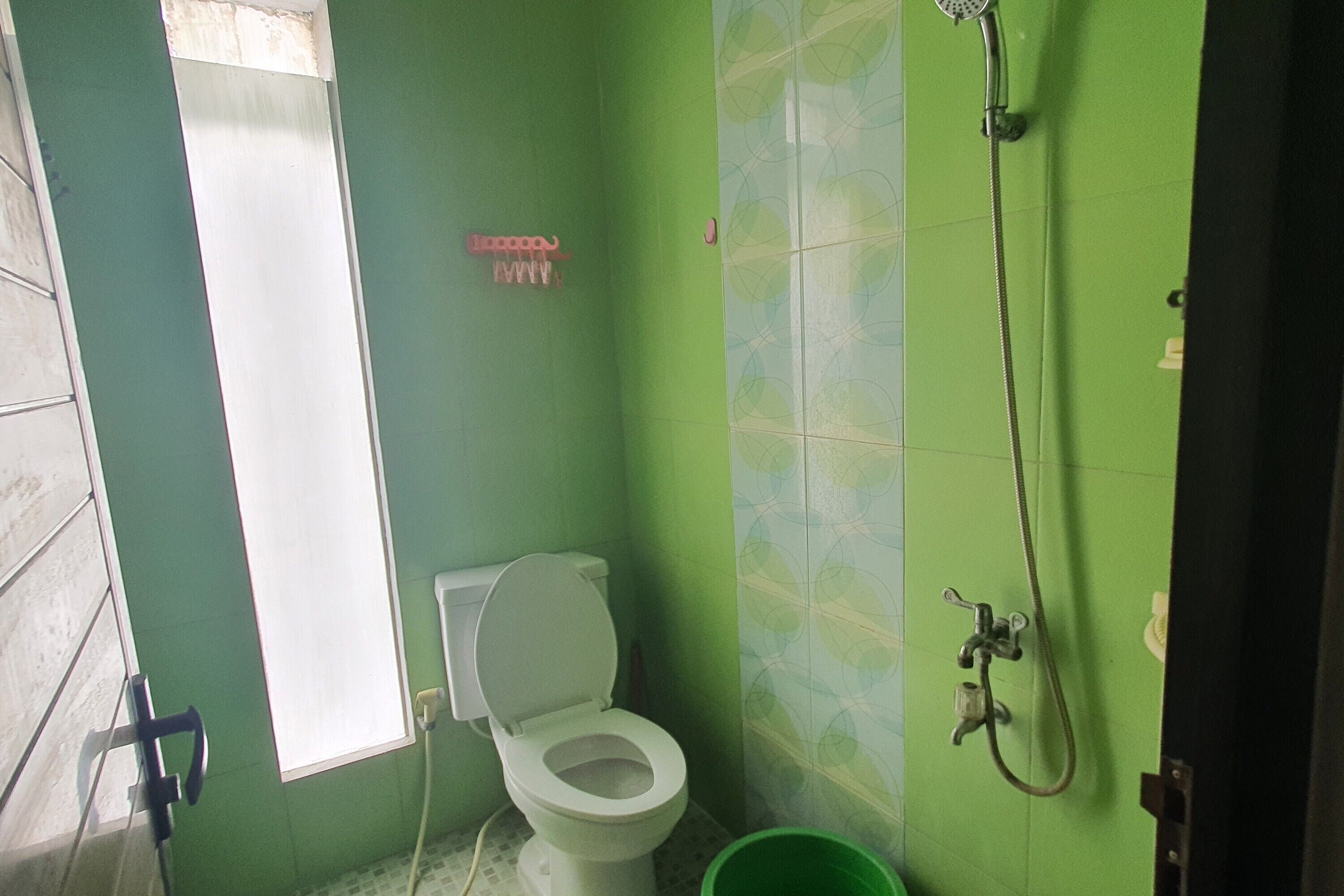 Une salle de bain avec des toilettes, une douche et un mur recouvert de carreaux verts.