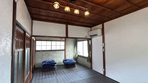 A room with tatami flooring, a traditional sliding door, and a ceiling with wooden beams and hanging lights. - Nano Inn (Okayama)