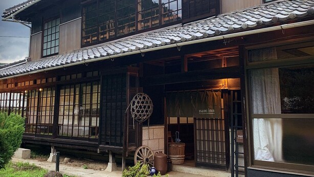 A traditional Japanese building with a tiled roof, wooden lattice windows, and a sign for 'nara inn.' - Nano Inn (Okayama)