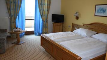 Ein Hotelzimmer mit einem hölzernen Bett, einem Fernseher auf einem Holzständer, einem kleinen Tisch mit einer Lampe und einem Fenster mit blauen Vorhängen.
