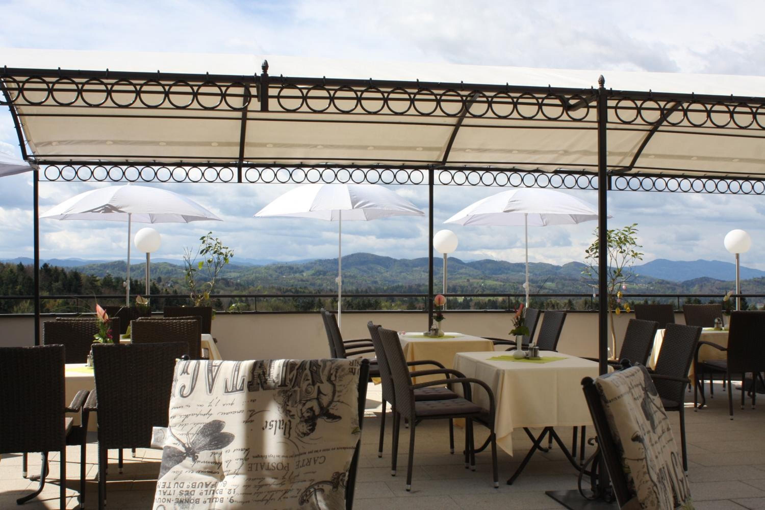 An outdoor dining area with tables and chairs, umbrellas, and a scenic mountain view.