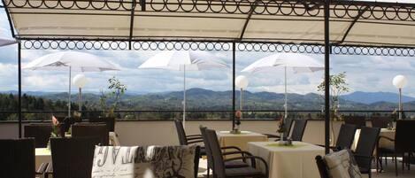 An outdoor dining area with tables and chairs, umbrellas, and a scenic mountain view.
