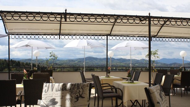 Un área de comedor al aire libre con mesas, sillas, sombrillas y una vista panorámica de la montaña.
