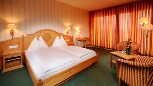 Habitación de hotel con cama doble, dos mesitas de noche, un escritorio, una silla y un ventanal con cortinas.