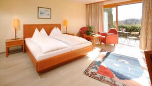 Habitación de hotel con una cama grande, dos lámparas de noche, una mesita con una silla, vistas al exterior y un amplio ventanal con cortinas.