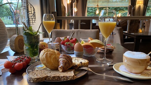 A breakfast table with croissants, bread, eggs, and fruit. - De Stobbe hotel & suites (Ruinen)