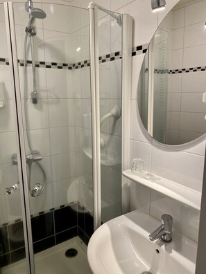 A modern bathroom with a glass-enclosed shower, a white sink, and a mirror above it. - De Stobbe hotel & suites (Ruinen)
