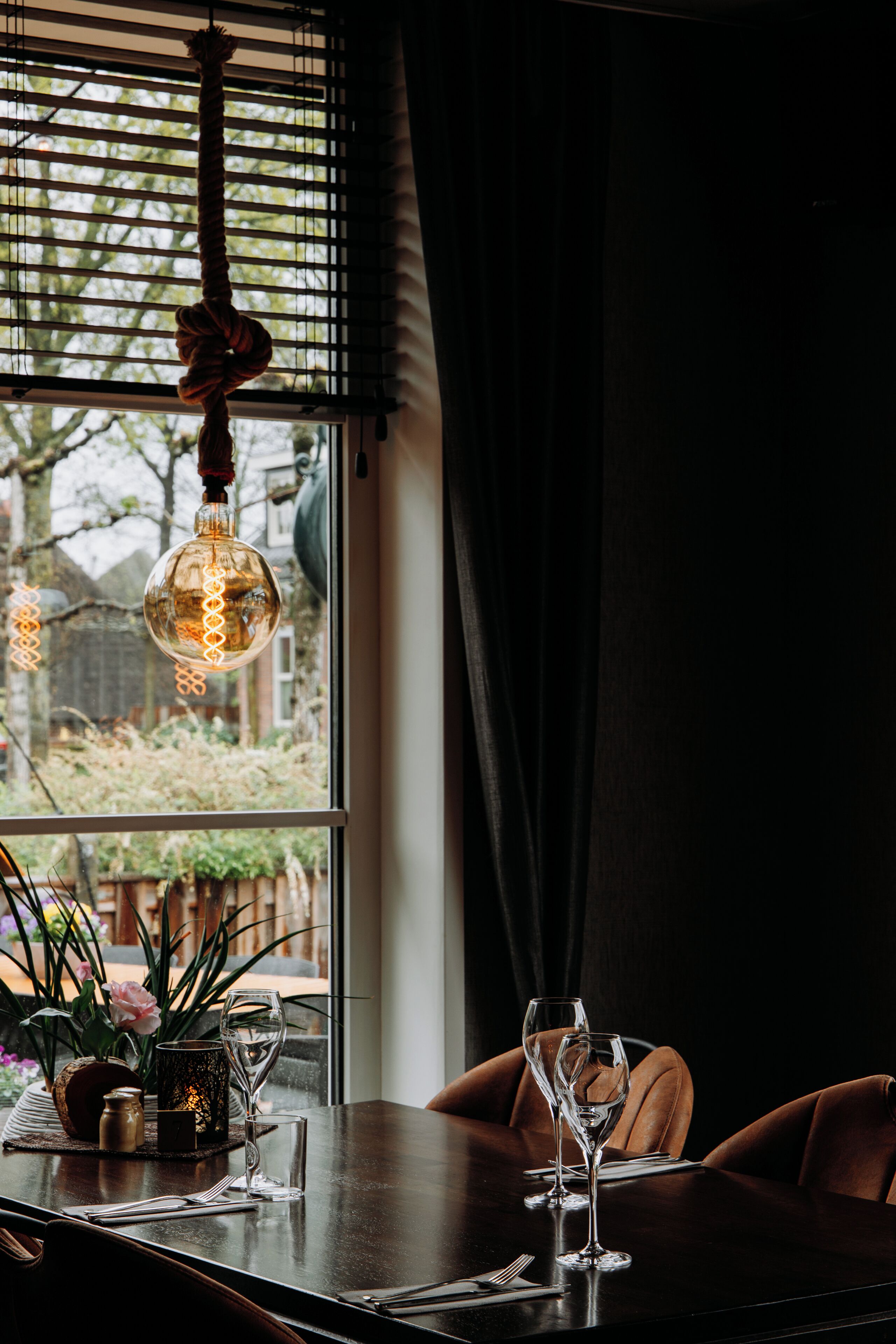 A dining table with two wine glasses, a candle holder, and a vase with flowers.