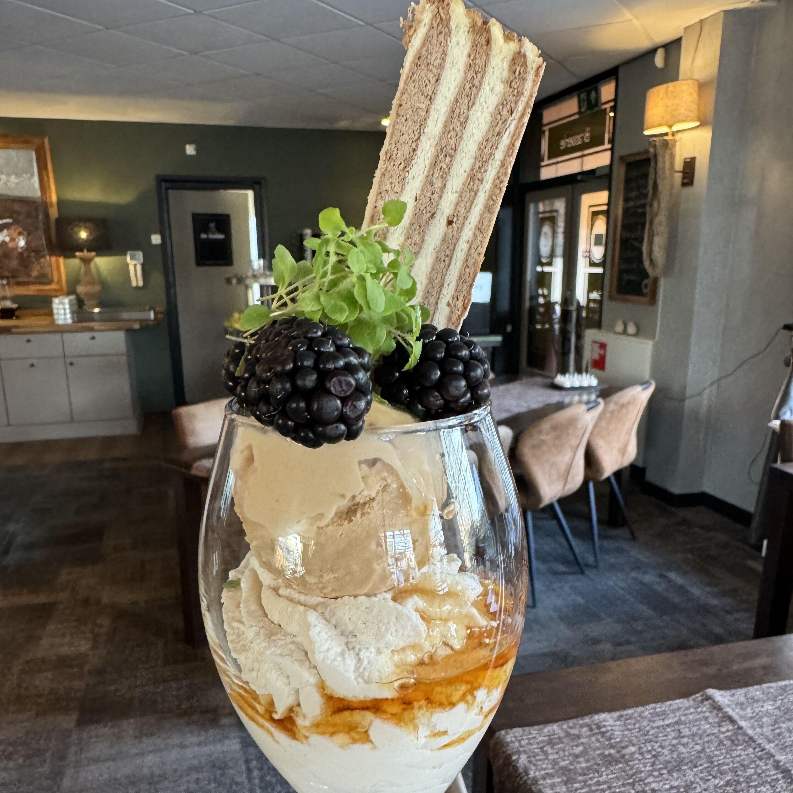 A dessert in a glass with ice, topped with whipped cream, blackberries, and a piece of cake.
