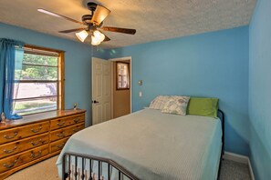 Un dormitorio con cama, cómoda, ventilador de techo y ventana con cortinas.