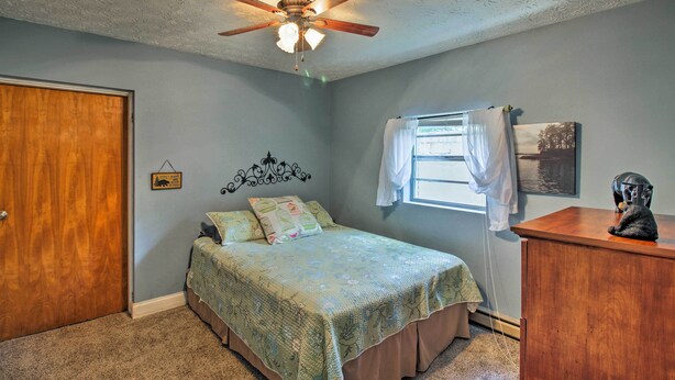 Un dormitorio con cama, ventilador de techo, puerta de madera, ventana con cortinas y cómoda con una escultura.