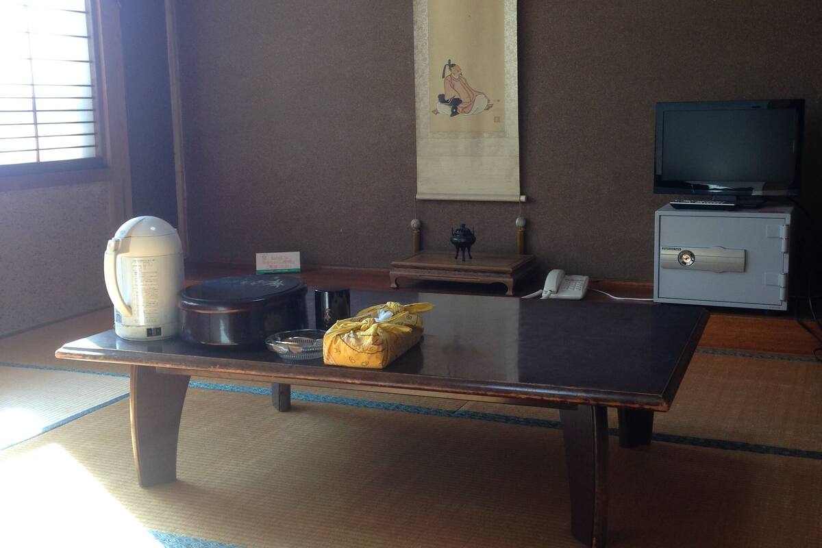 A traditional Japanese room with tatami flooring, a low table, a television, and a large scroll on the wall.