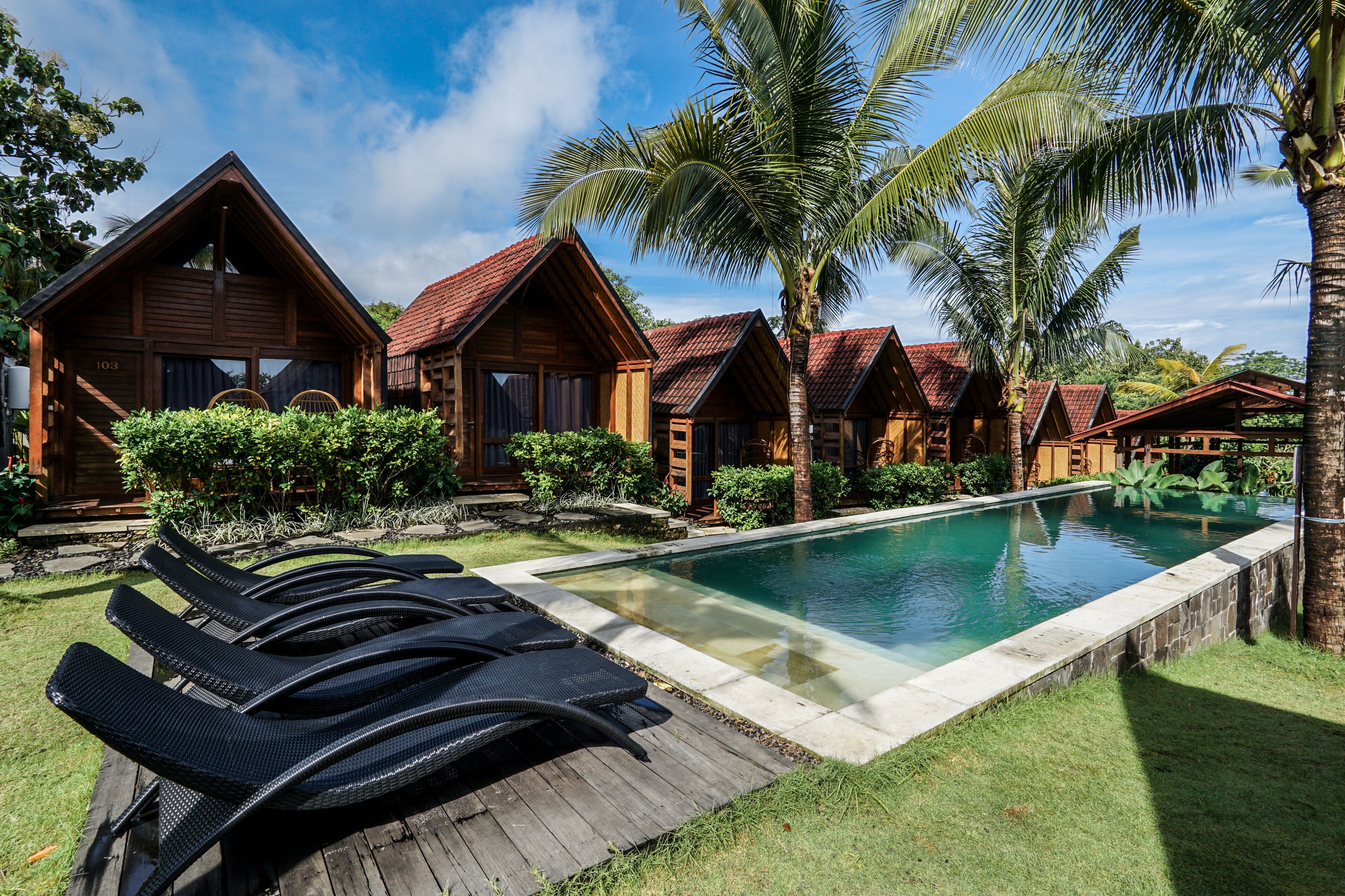 A resort with wooden cabins, a swimming pool, and lounge chairs.