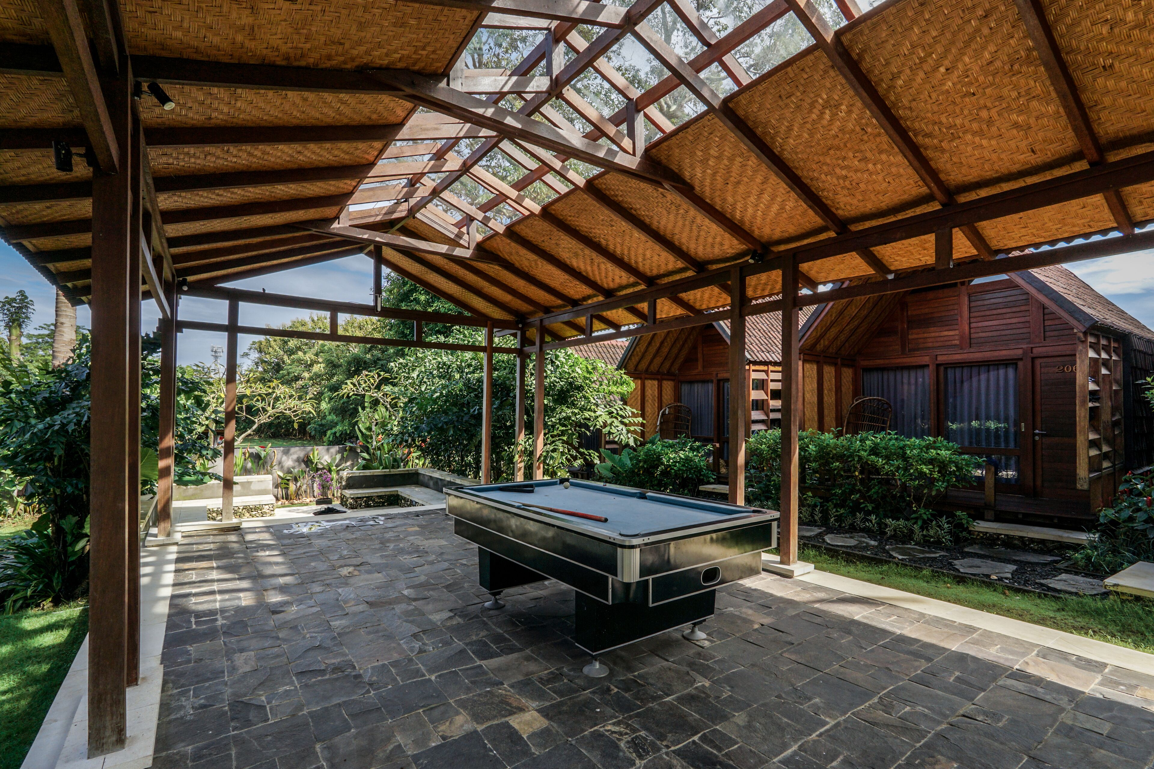 Une table de billard se trouve dans un espace extérieur abrité, surmonté d’une structure en bois.
