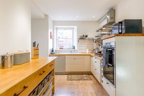 A compact kitchen with a wooden countertop, a built-in oven, and a window providing natural light. - House On The Harbour | Pittenweem (Pittenweem)