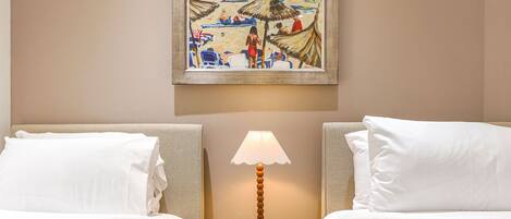 Een hotelkamer met twee bedden, een nachtkastje met een lamp en een schilderij aan de muur.