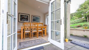 An open door leading to a dining area with a table and chairs, framed artwork on the wall, and a garden view.