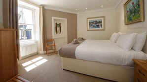 Une chambre à coucher avec un grand lit, une commode en bois, une chaise et une fenêtre avec des rideaux.
