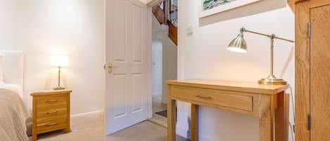 A hallway with a wooden desk, a lamp, a door, and a painting on the wall.