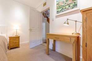 A hallway with a wooden desk, a lamp, a door, and a painting on the wall. - House On The Harbour | Pittenweem (Pittenweem)