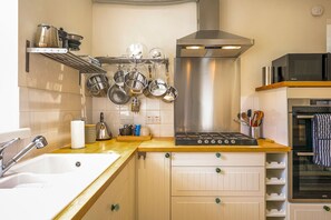 A kitchen with a stove, oven, microwave, and hanging pots. - House On The Harbour | Pittenweem (Pittenweem)