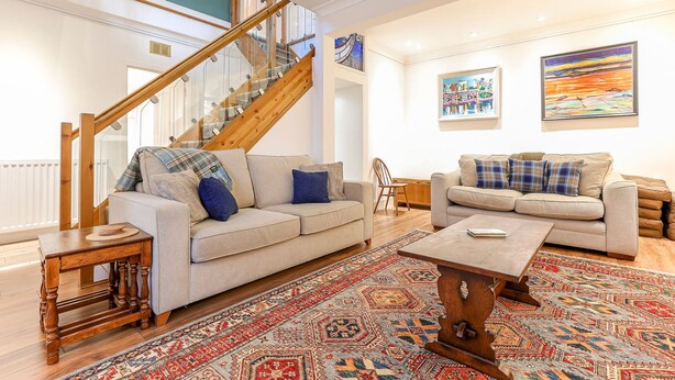 A spacious living room with a staircase, two sofas, a coffee table, and a patterned rug.