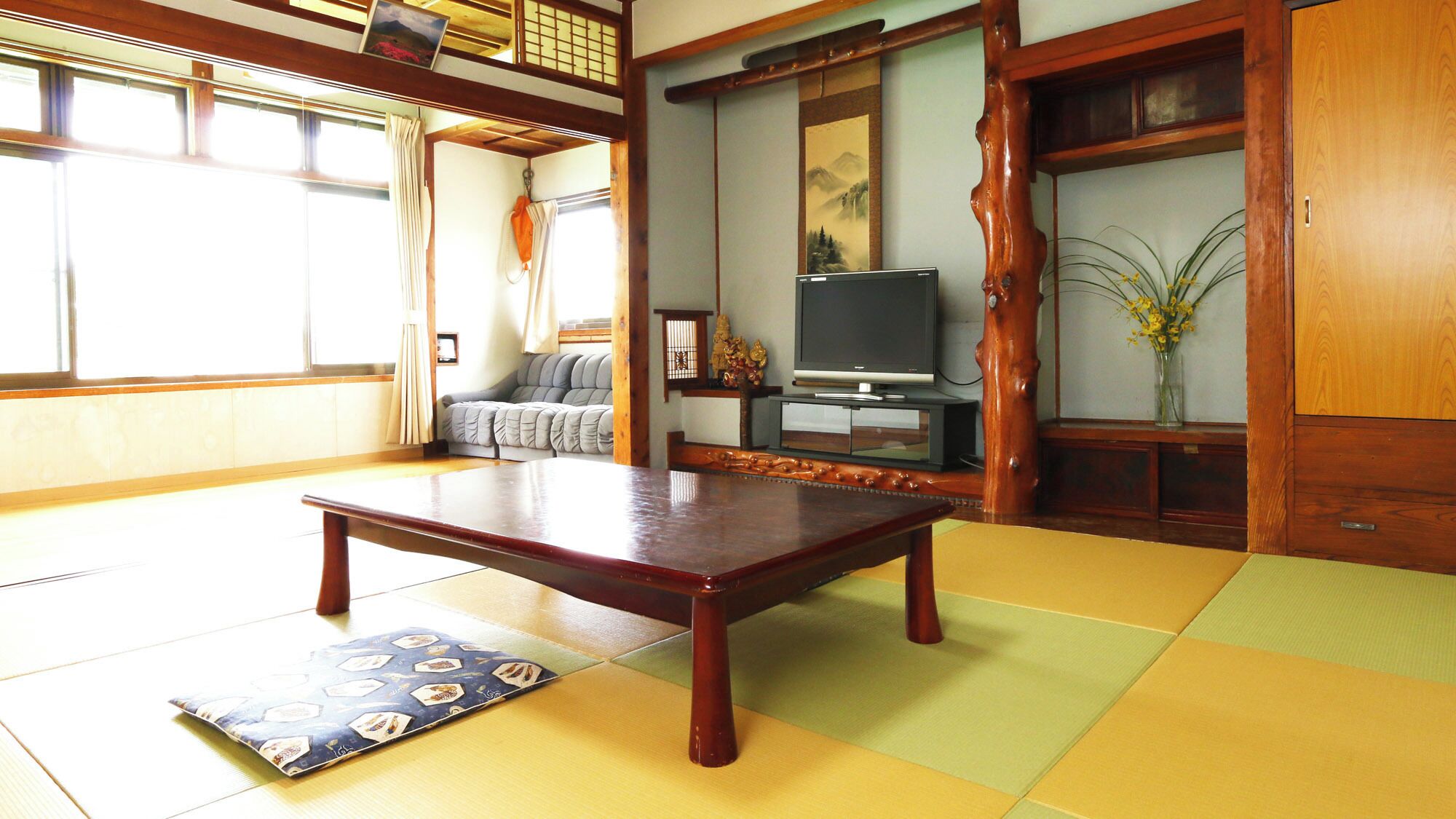 Una habitación con tatamis, una mesa de madera baja, un sofá, un televisor y una puerta corredera tradicional japonesa.