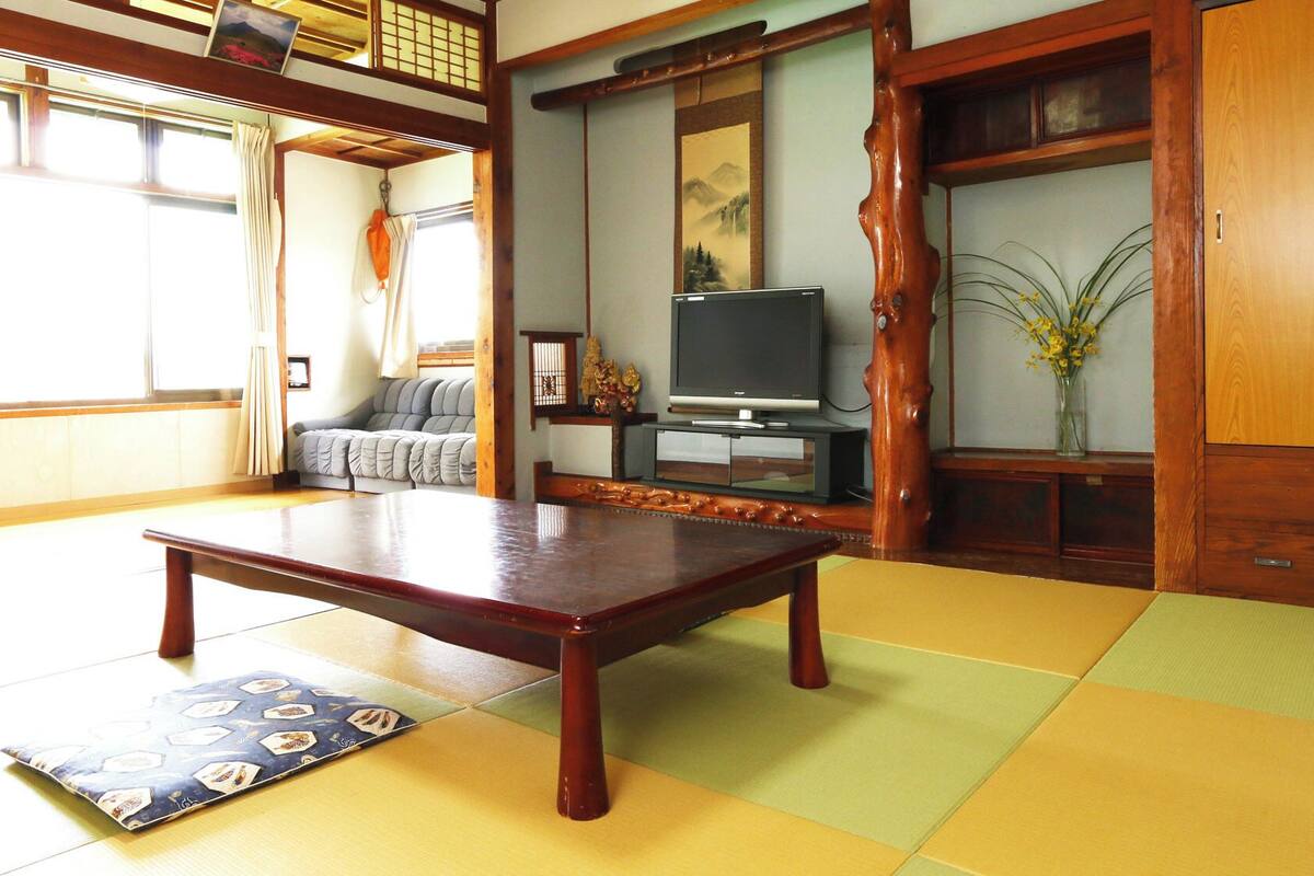 A tatami mat room with a low wooden table, a sofa, a television, and a traditional Japanese sliding door.