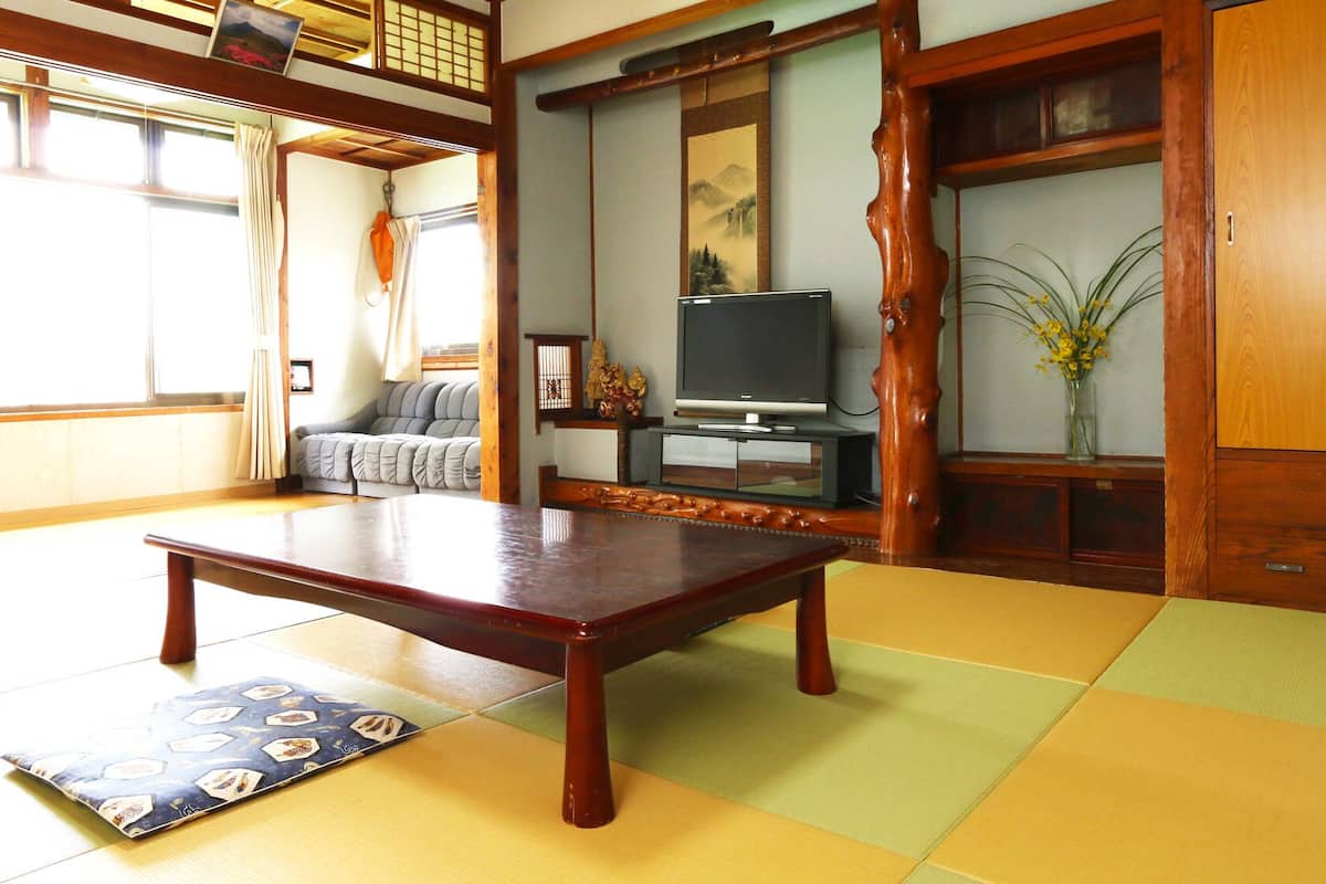 A tatami mat room with a low wooden table, a sofa, a television, and a traditional Japanese screen.