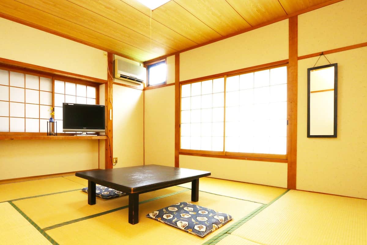 A traditional Japanese room with tatami flooring, a low table, a television, and a mirror.