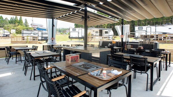 An outdoor dining area with tables and chairs, a grill station, and a view of RVs in the background. - Franping Village Aso (Aso)