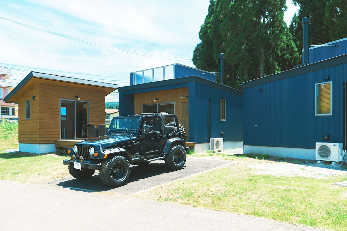 A black SUV parked in front of a blue building with a small wooden structure nearby.