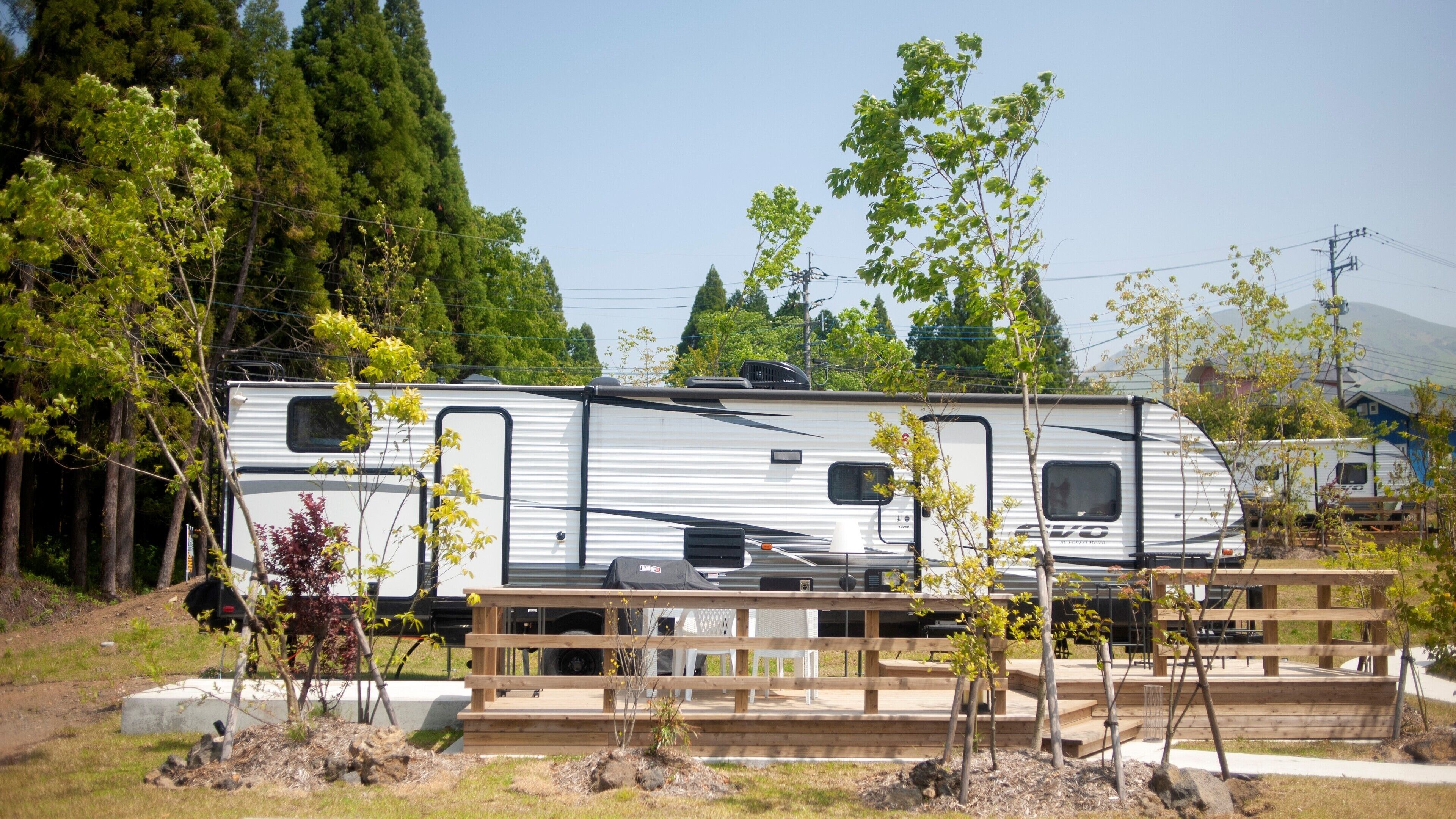 A recreational vehicle (RV) parked in a campsite with a wooden deck and picnic tables.