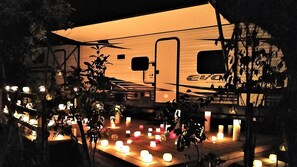 Un camping-car moderne doté d’un intérieur spacieux, éclairé par de nombreuses bougies disposées sur le sol, et entouré d’arbres.