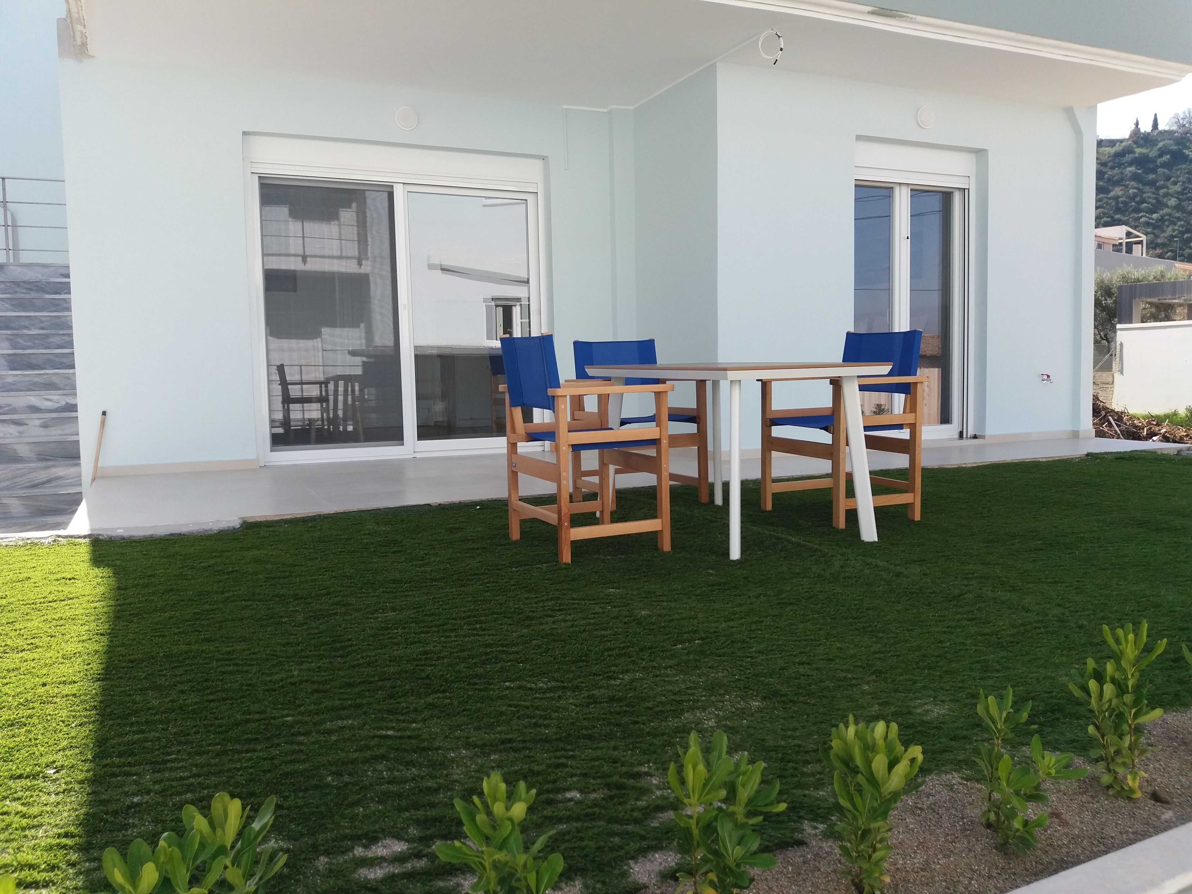 Una casa moderna con un patio, una mesa de comedor con sillas y un césped bien cuidado.