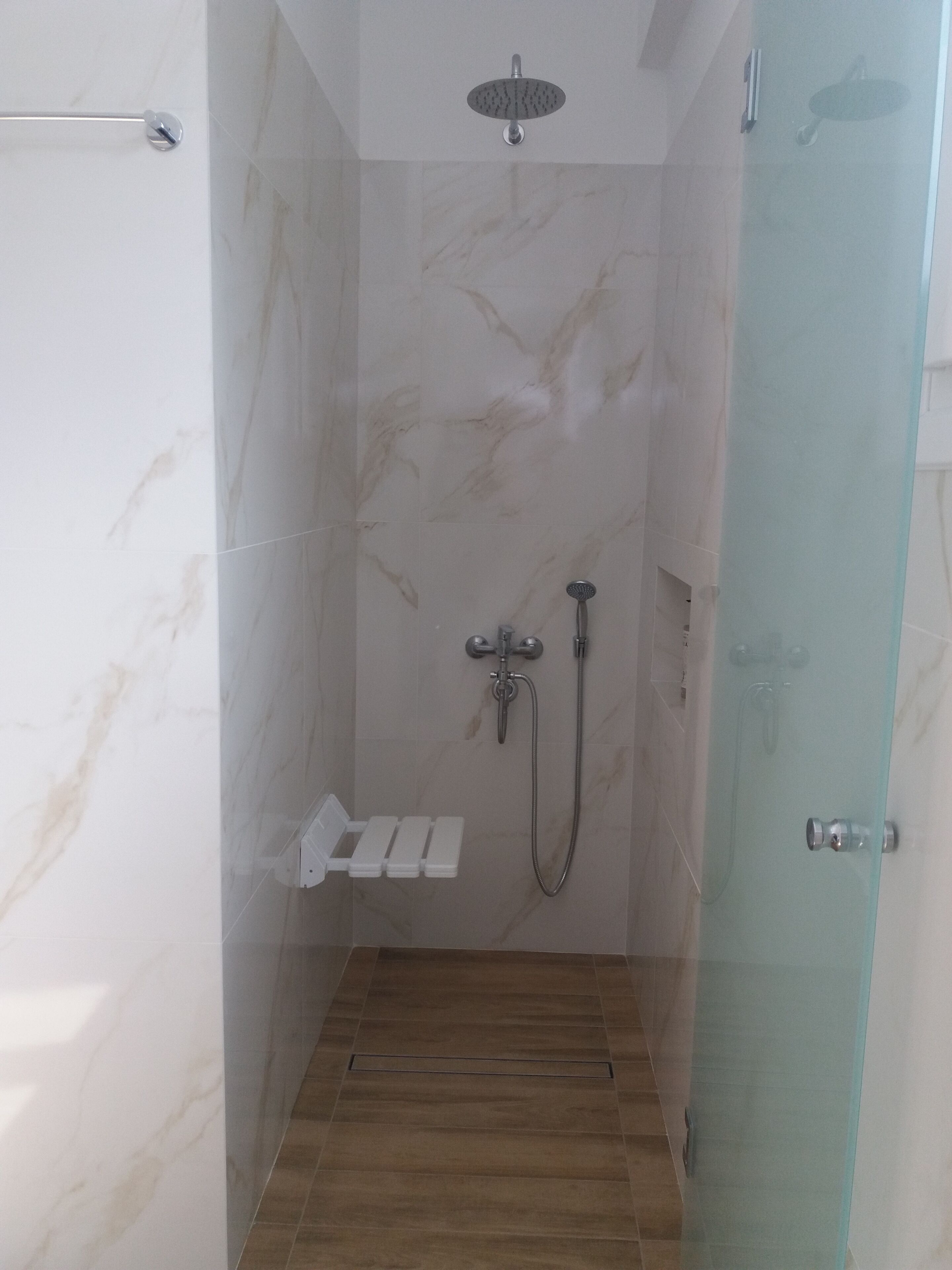 A small, enclosed shower area with a glass door, a handheld showerhead, a wall-mounted faucet, and a shelf with toiletries.