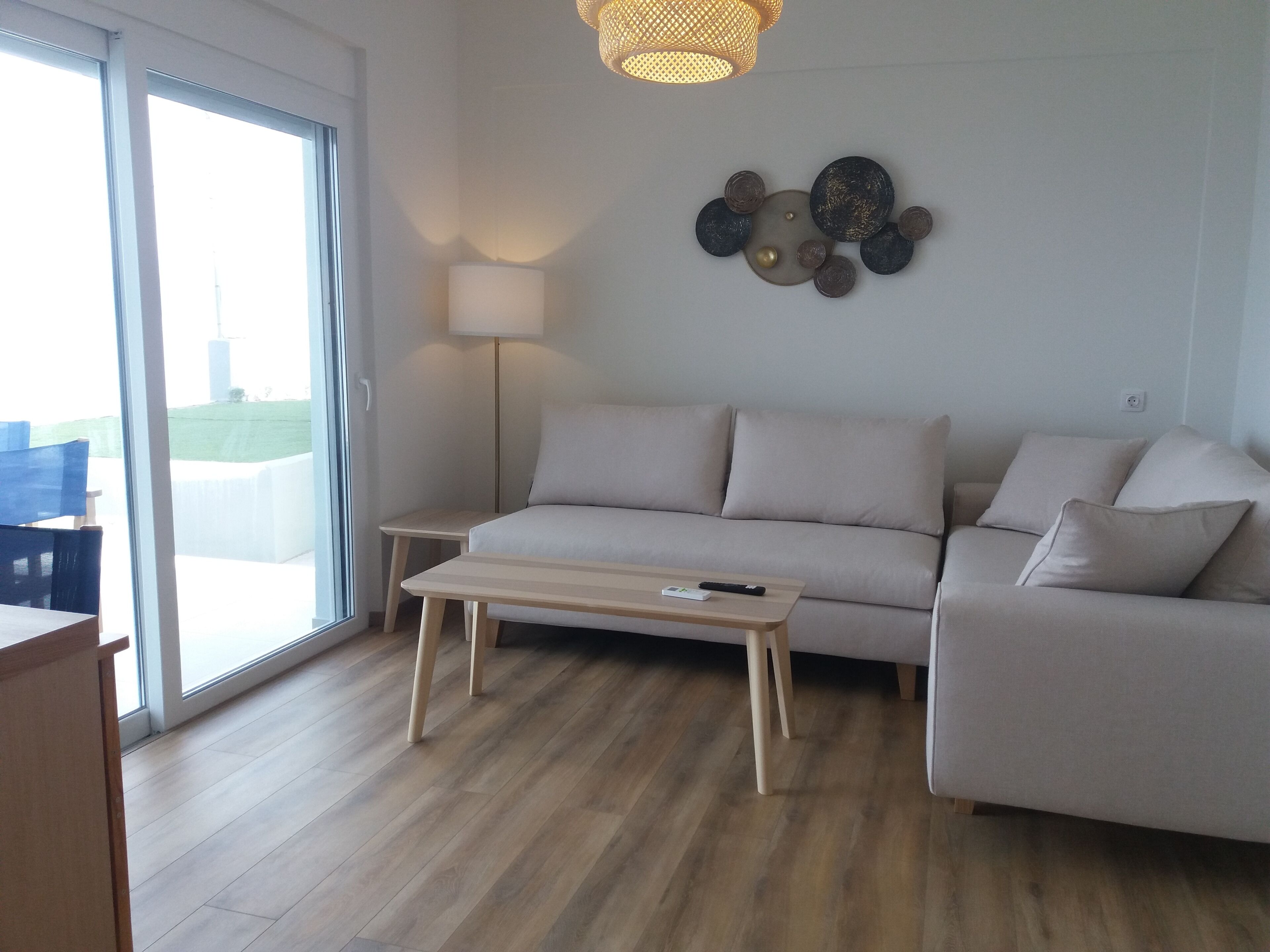 Una sala de estar moderna con un sofá, una mesa de centro y una lámpara. Un ventanal grande proporciona luz natural.