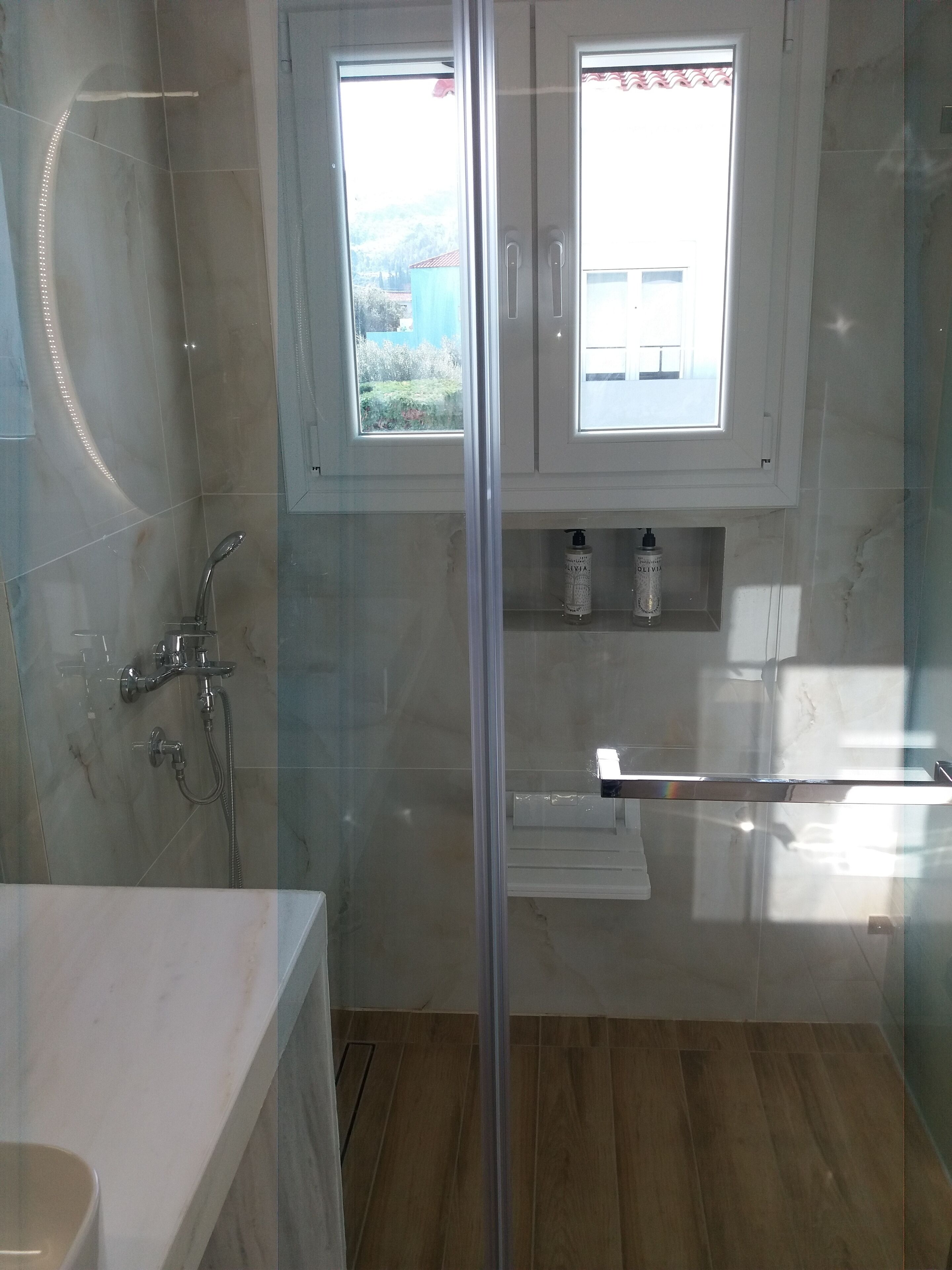 A modern bathroom with a glass-enclosed shower, a bathtub, and a window above the sink.