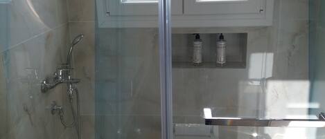 A modern bathroom with a glass-enclosed shower, a bathtub, and a window above the sink.