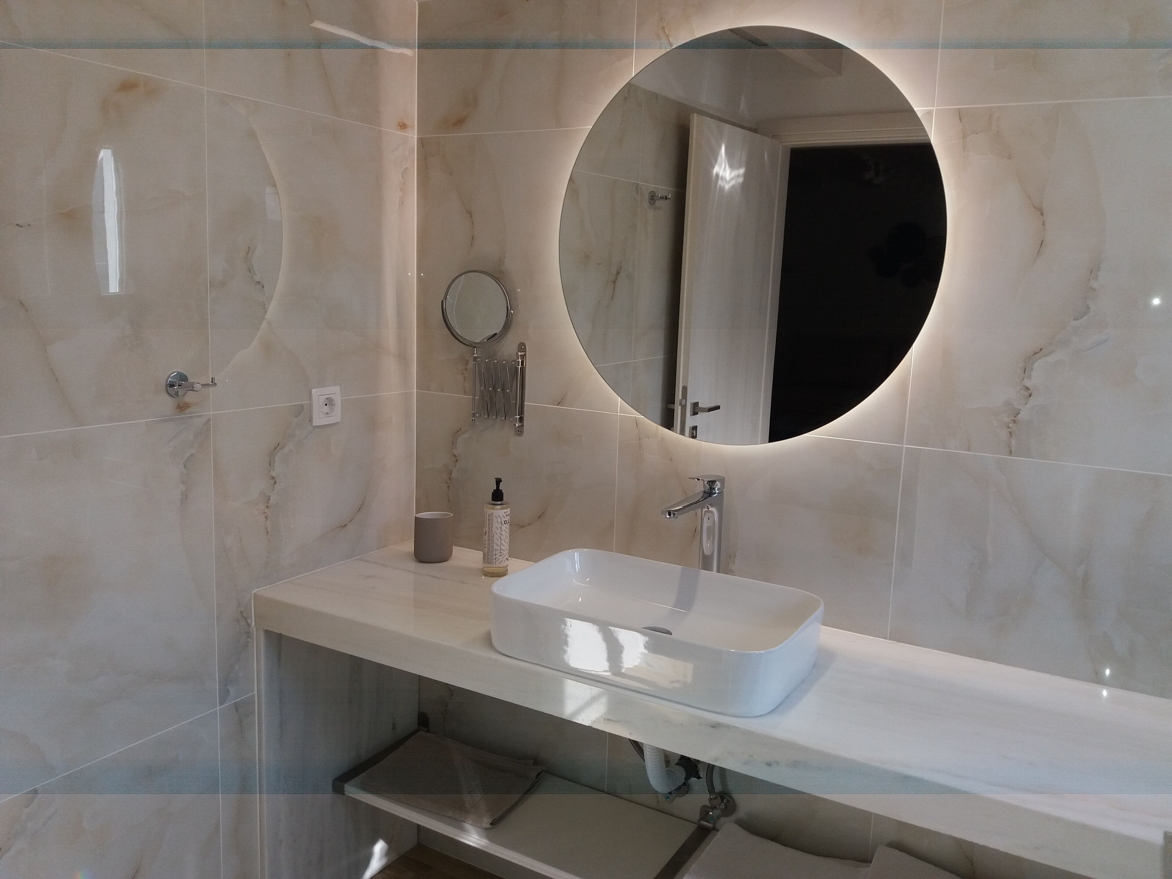 Een moderne badkamer met een marmeren wastafelmeubel, een ronde spiegel en een handdouche.