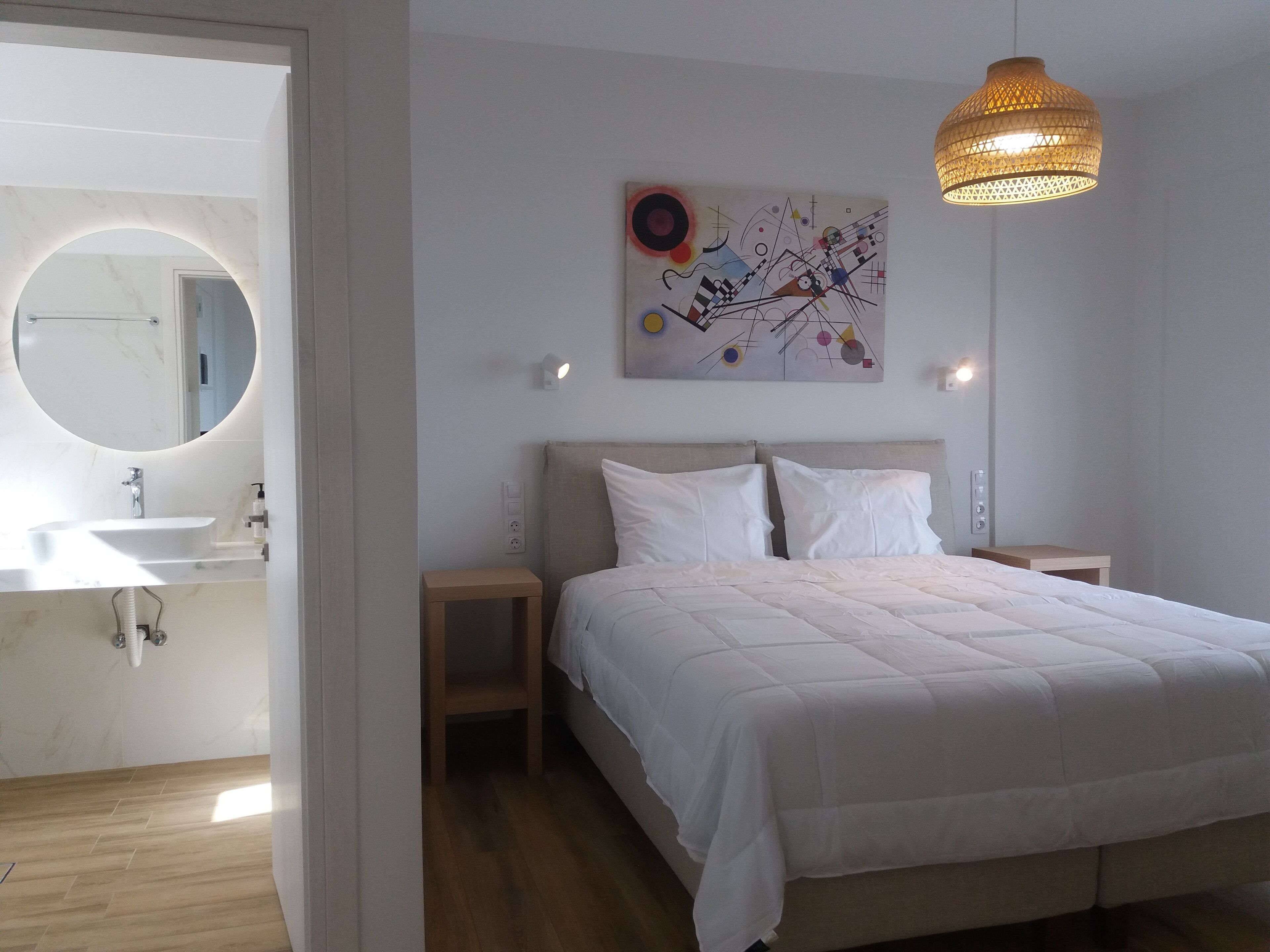 A bedroom with a bed, a bedside table, a nightstand, a wall-mounted light, and a hanging light fixture.